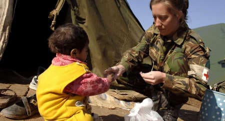 Pakistan, 2006: A Dutch nurse from the NATO Military Relief Hospital at Chaklala Air Base distributes sweets to a young earthquake victim in the camp of the &quot;Humanity First&quot; relief organisation (© SHAPE)
)