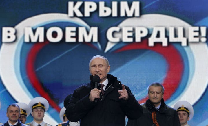 Le président russe Vladimir Poutine, à l’avant-plan, s’adresse au public venu assister au concert « Nous sommes ensemble », organisé pour célébrer le rattachement de la Crimée à la Russie, en présence, à l’arrière-plan, du premier ministre de la Crimée, Sergueï Aksionov, et du président de l’Assemblée nationale de Crimée, Vladimir Konstantinov (à gauche), sur la place Rouge, au cœur de Moscou, le 18 mars 2014. À l’arrière-plan, on peut lire « La Crimée est dans mon cœur ! ». © Reuters
)