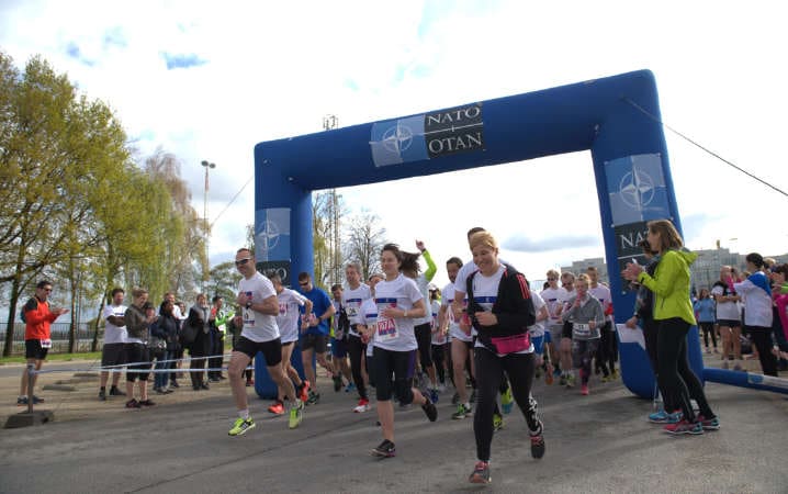 Participants cross the finish line of NATO’s “She Runs, He Runs, We Run” mixed relay event, which brings together participants of all ages and ranks, as well as their family members – 2017. © NATO
)