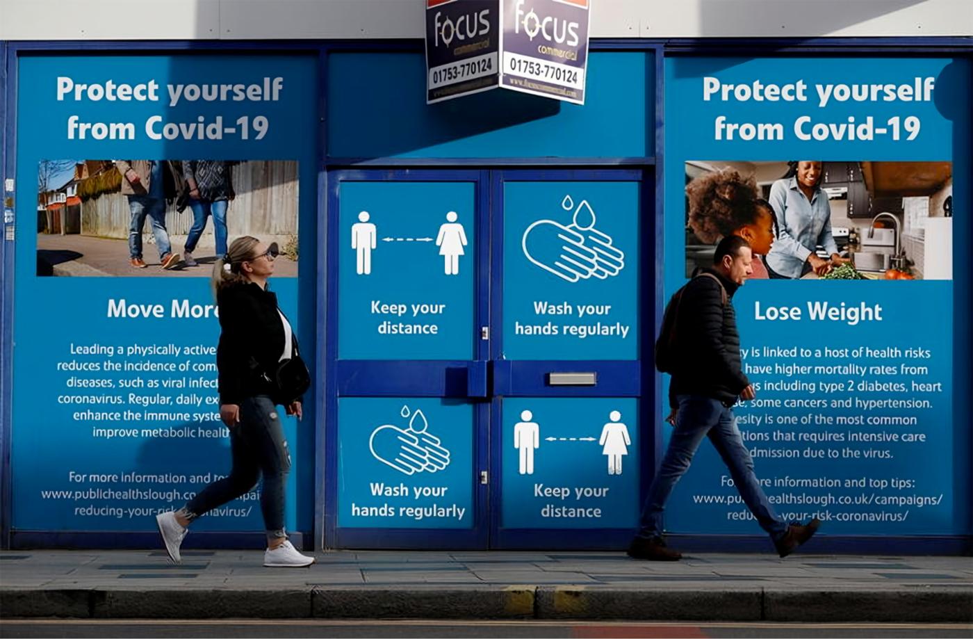 People walk past signage about COVID-19 measures in Slough, Great Britain. © Reuters
)