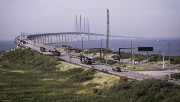 Колона британської армії перетинає Ерезундський міст, який поєднує Данію зі Швецією, на своєму двохтисячно кілометровому шляху в Голландському Гуку до Норвегії для участі в навчаннях НАТО «Трайдент джанкче  - 2018». Демонстрація спроможності швидко переправляти і утримувати збройні сили країн Альянсу до Європи і по Європі була важливим елементом навчань. © NATO
)