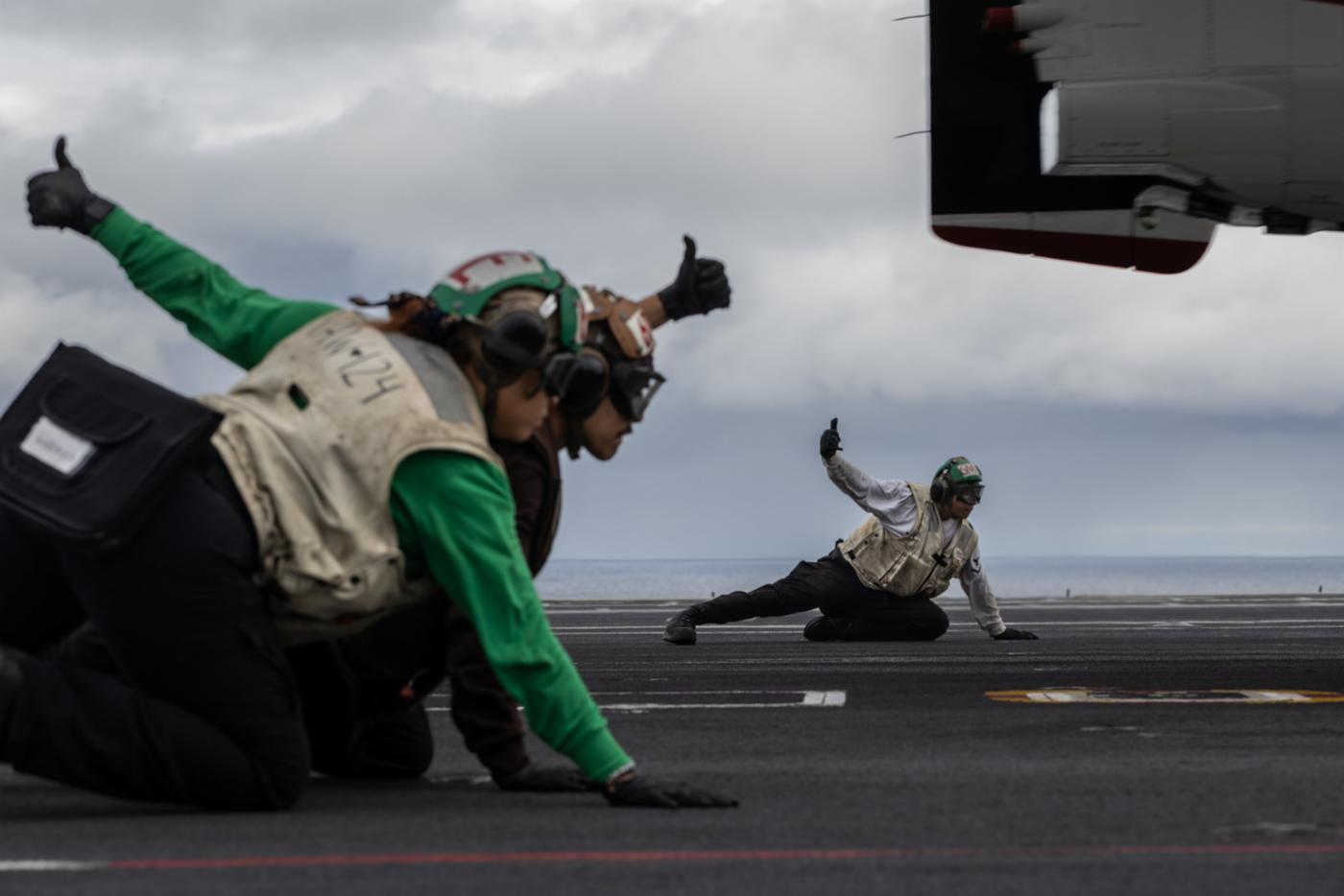 US Navy sailors brace themselves as an E-2D Hawkeye surveillance aircraft takes off from the deck of the USS Gerald R. Ford.
)