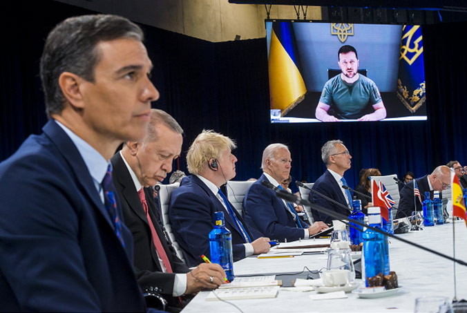 Spanish Prime Minister Pedro Sánchez, Turkish President Recep Tayyip Erdoğan, then UK Prime Minister Boris Johnson, US President Joe Biden and NATO Secretary General Jens Stoltenberg listen to Ukrainian President Volodymyr Zelenskyy as he addresses the North Atlantic Council at the NATO Summit in Madrid. Photo by NATO photographer.