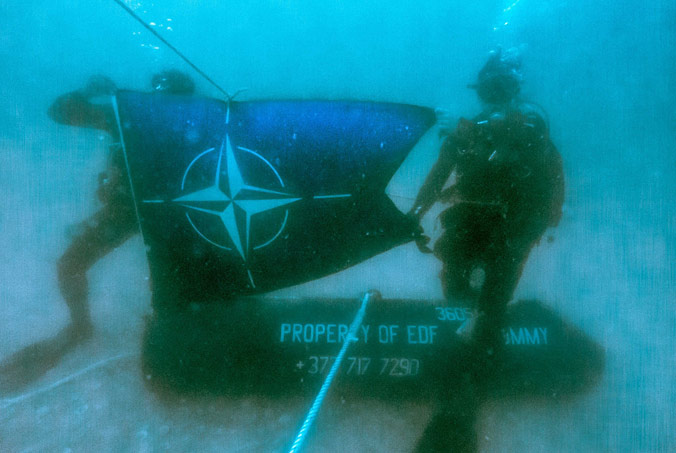 Two divers hold up the NATO flag in the waters of the English Channel during a historical ordnance disposal operation off the coast of Dieppe, France. Led by Standing NATO Mine Countermeasures Group 1, the operation successfully removed 13 pieces of historical ordnance, reducing the risk of mine encounters in the water and making the area safer for all mariners. Photo by Allied Maritime Command.