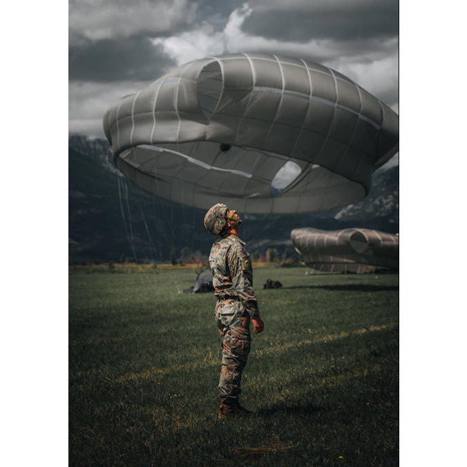 A US Army paratrooper assigned to the 173rd Airborne Brigade looks up as fellow paratroopers descend towards him during an airborne operation on Frida Drop Zone, Pordenone, Italy. The 173rd Airborne Brigade is the US Army's Contingency Response Force in Europe, providing rapidly deployable forces to the United States European, African and Central Command areas of responsibility. The brigade routinely trains alongside NATO Allies and partners. Credit: US Army Sgt. Mariah Y. Gonzalez