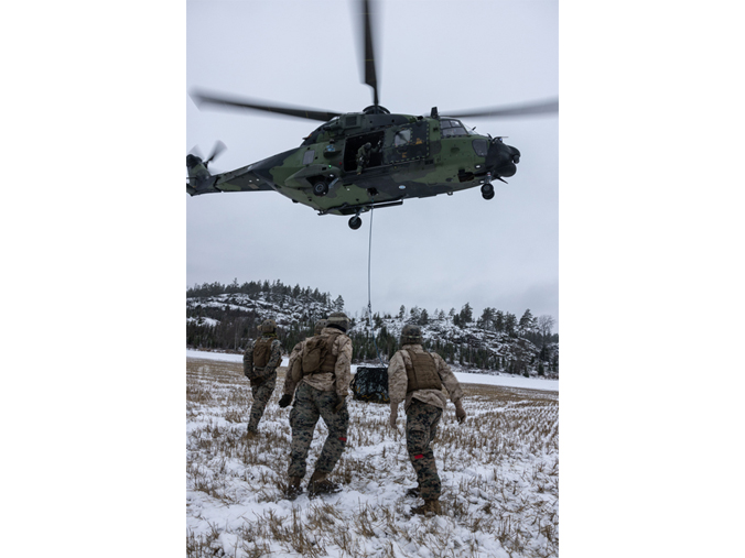 Des  marines américains observent un hélicoptère NH90 de la marine finlandaise  qui s'apprête à soulever un conteneur de vrac dans le sud de la Finlande.